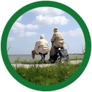 Twee oudere mensen zitten langs het water, met uitzicht op de zee.
