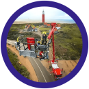 Brandweerman in een hoogwerker voor de vuurtoren van Texel, met uitzicht op duinen en zee.